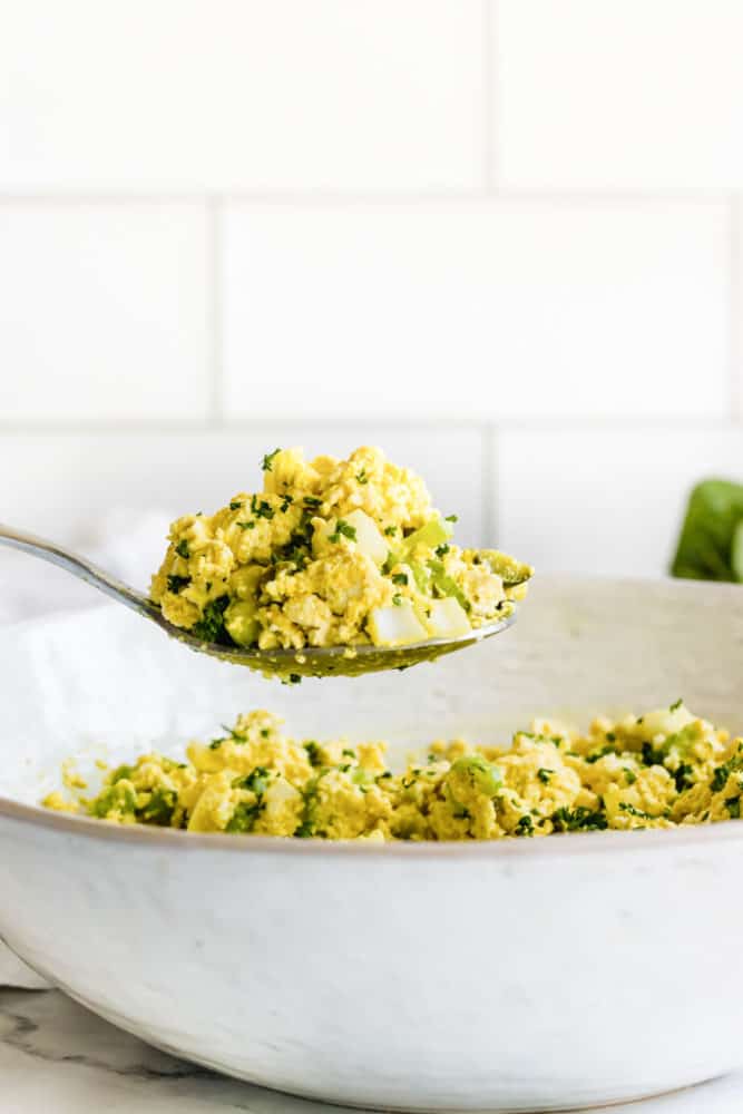 Spoonful of vegan eggless egg salad over a white bowl of vegan eggless egg salad. 