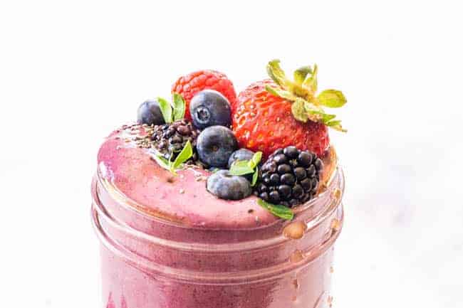 Close up of mixed berry smoothie in a jar topped with mixed berries. 