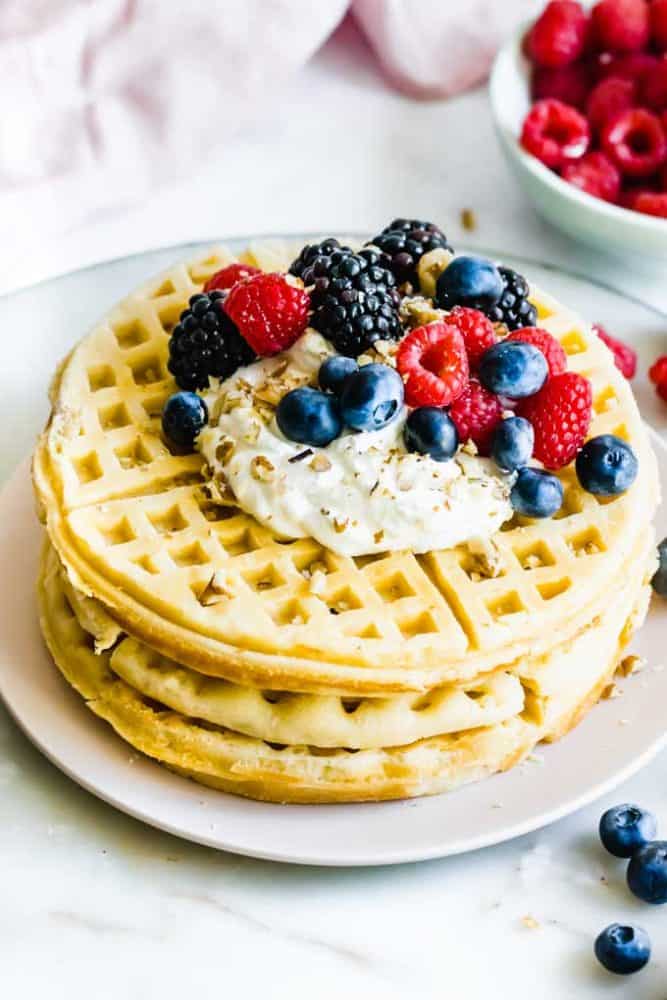 Stack of vegan waffles with vegan berries and cream on top.