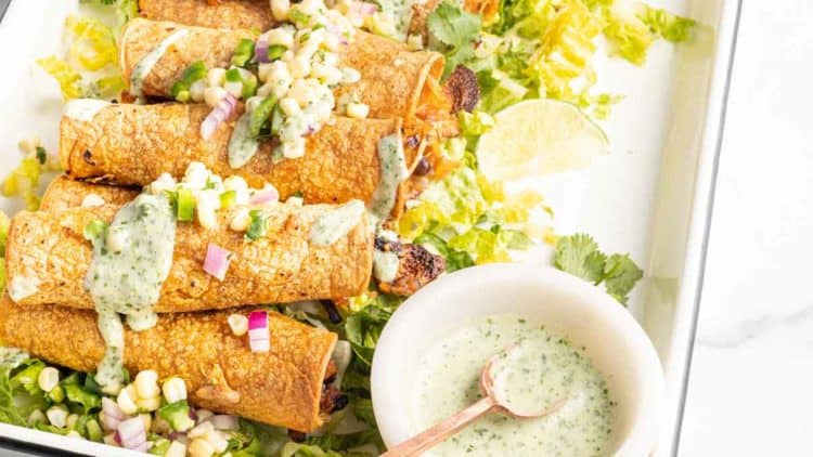 Dish of baked vegan taquitos with a side of cilantro lime crema. 