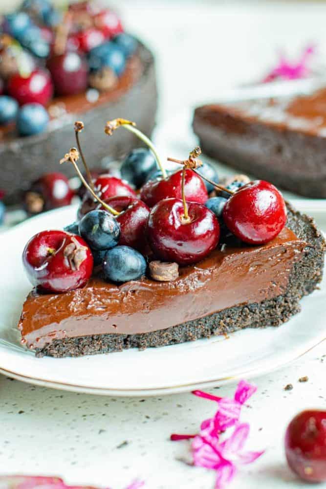 Slice of chocolate tart decorated with blueberries and cherries. 
