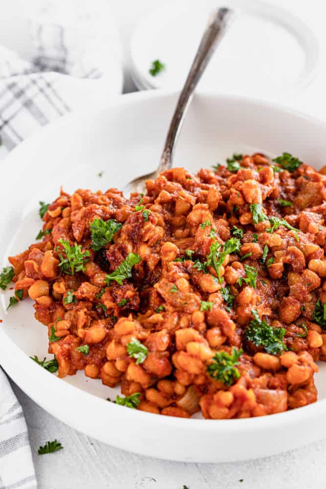white dish of vegan baked beans with a serving spoon. 