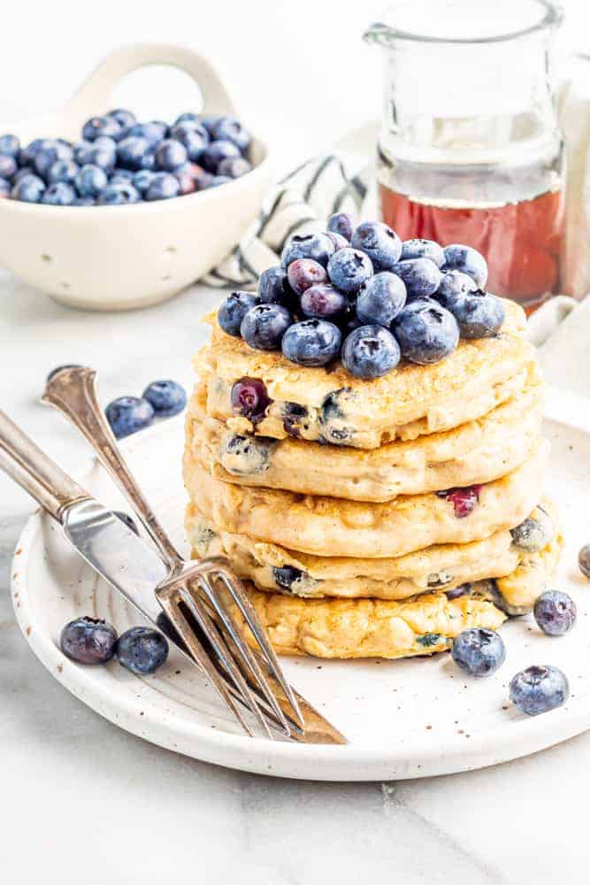 vegan blueberry pancakes topped with fresh blueberries on a plate with utensils