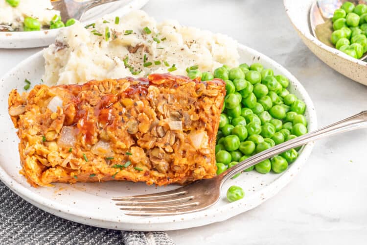 Plate with a fork and vegan meatloaf with a side of peas and mashed potatoes.