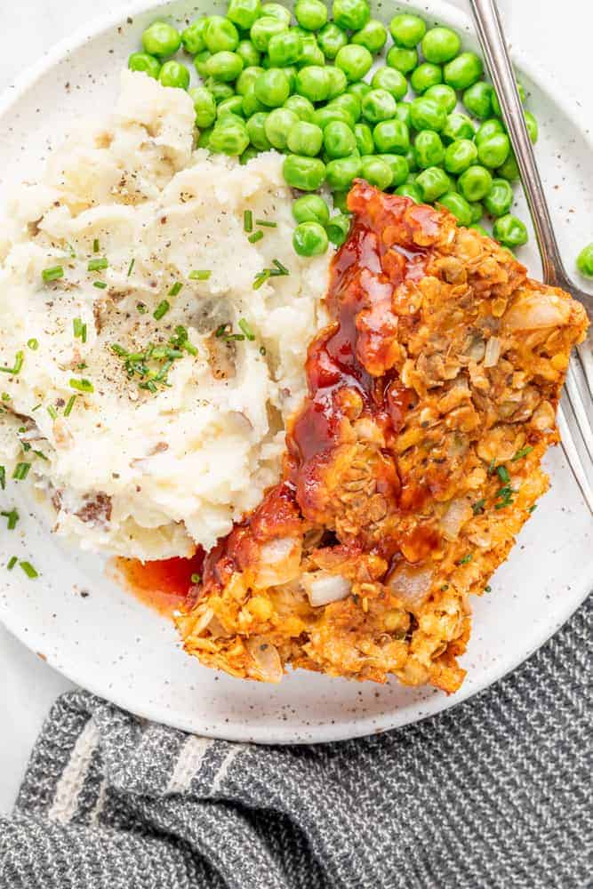 Plate of vegan meatloaf with a side of peas and mashed potatoes.