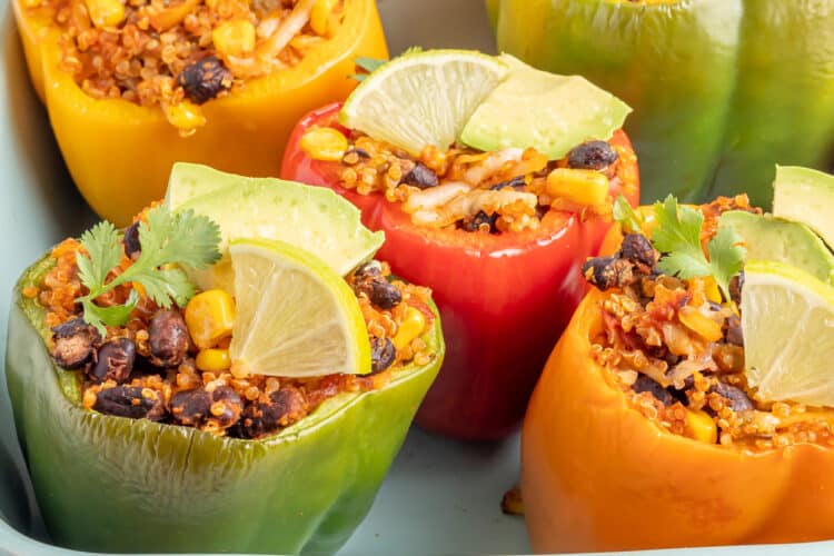 Dish of vegetarian stuffed peppers all garnished with avocado, lemons, and cilantro.