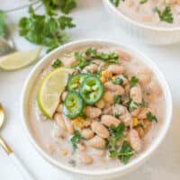 2 bowls of white bean soup garnished with lime, jalapeno, and cilantro