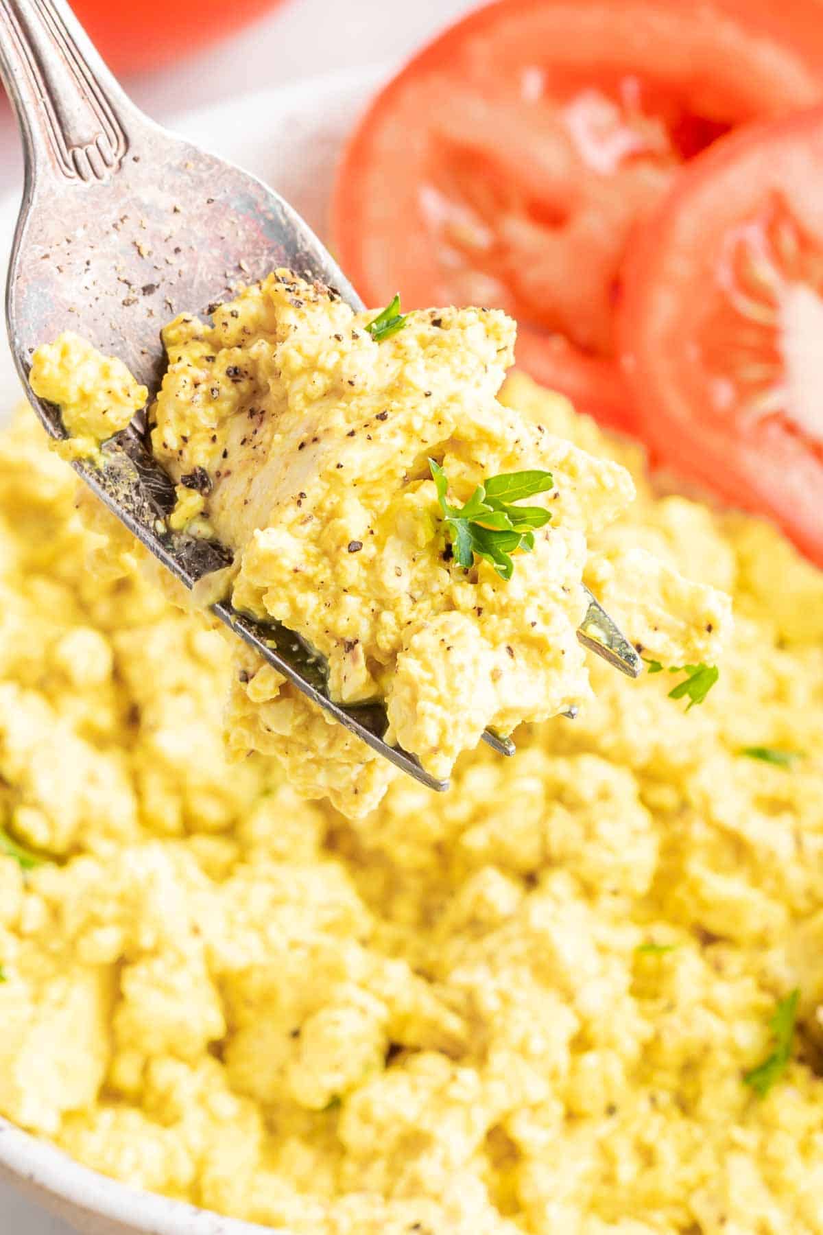 close up bite of the vegan scrambled eggs with a garnish of parsley and tomato slices