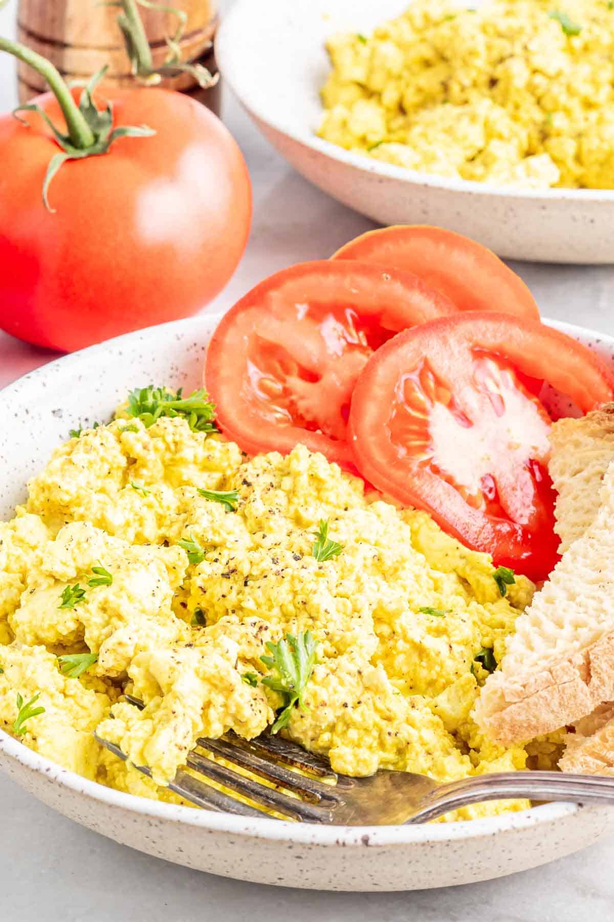 a plate of vegan tofu scrambled eggs with fresh tomatoes on the side 