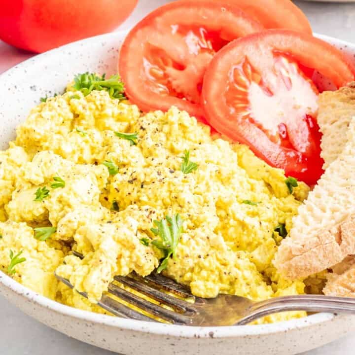 vegan scrambled eggs with chopped parsley and slices of tomatoes on a plate