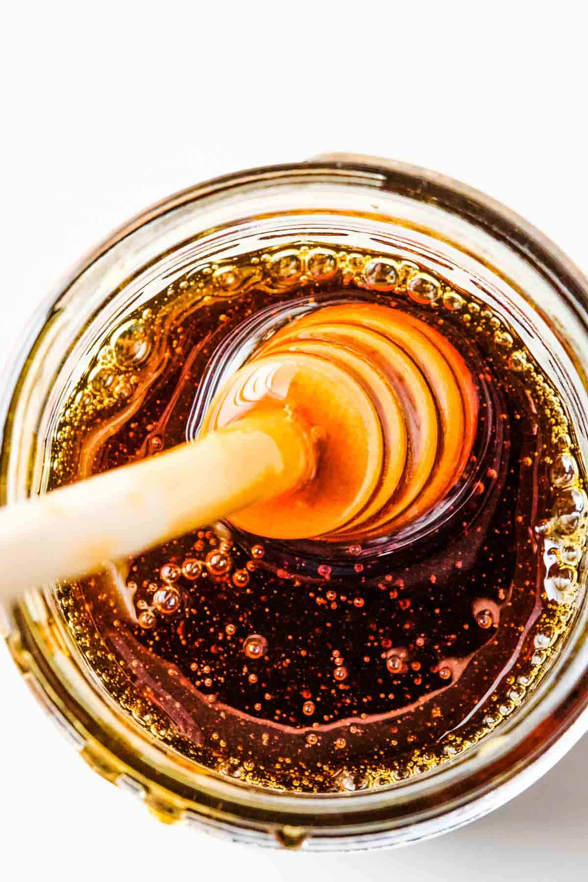 an overhead image of honey in a jar with honey dipper in the honey.