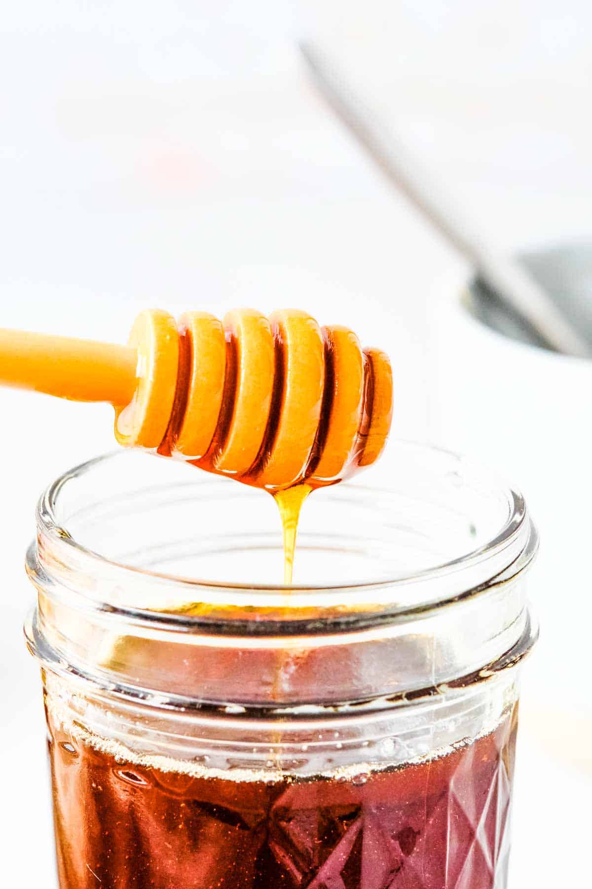 a jar of vegan honey with a honey dipper dripping above.