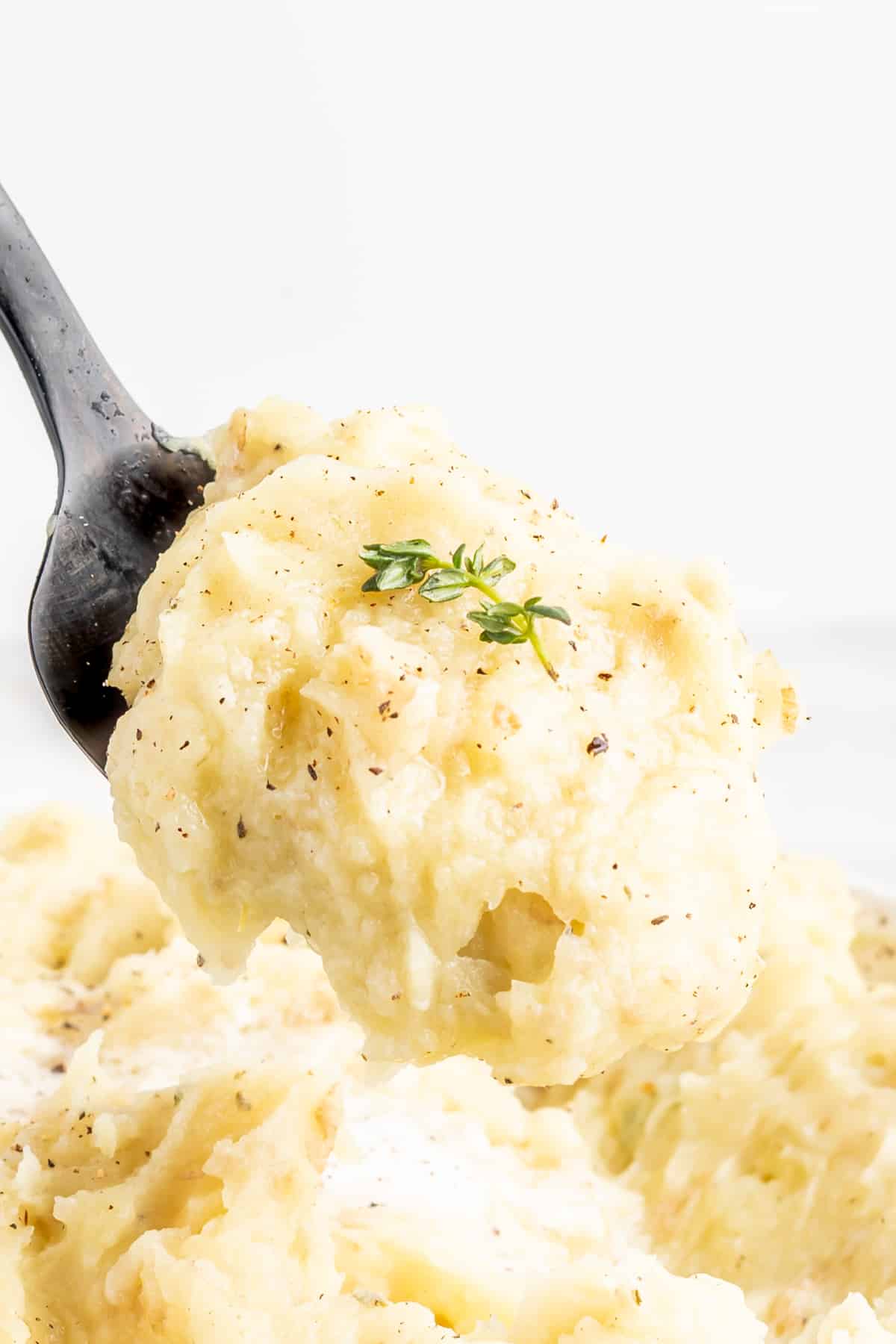 a close up spoonful of vegan mashed potatoes topped with fresh herb garnish.