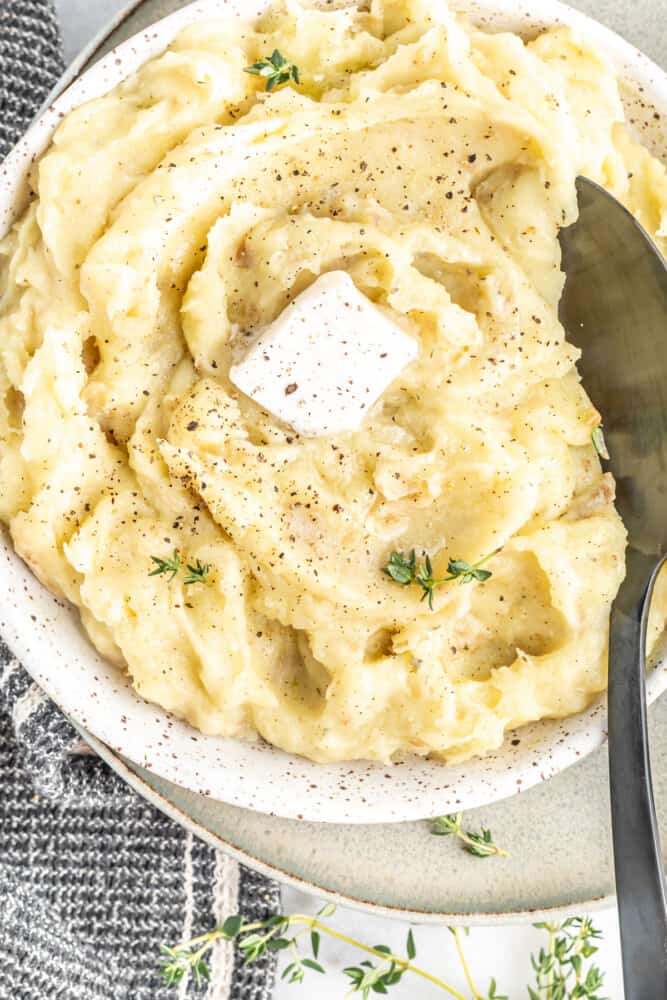 a bowl of creamy smooth dairy free vegan mashed potatoes with a pat of butter and fresh herbs.