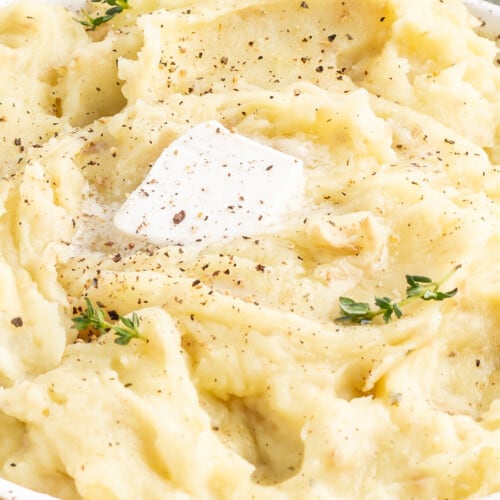 a dish of creamy smooth vegan mashed potatoes topped with a pat of butter and fresh herbs