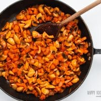 mushrooms and tomato paste added to sauteed vegetables in a black skillet with a wooden spoon stirring.