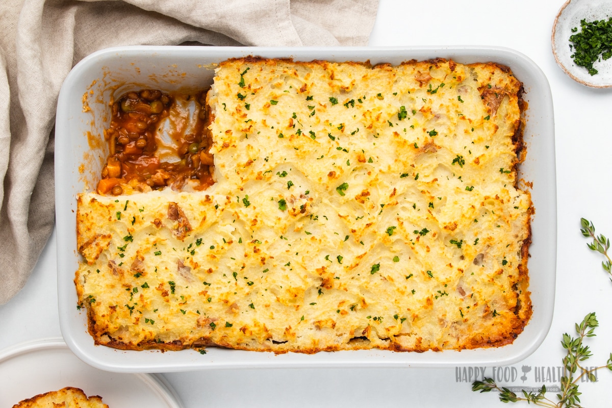 baked vegan lentil shepherds pie in a white rectangular dish. One piece has been removed from the top left corner.