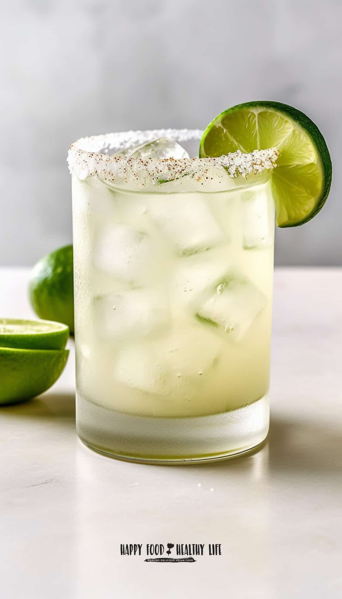 picture of a clear glass filled with an off white liquid and ice cubes, salt and brown on rim with a lime wheel on the rim. Cut limes to the side. appears to be a margarita