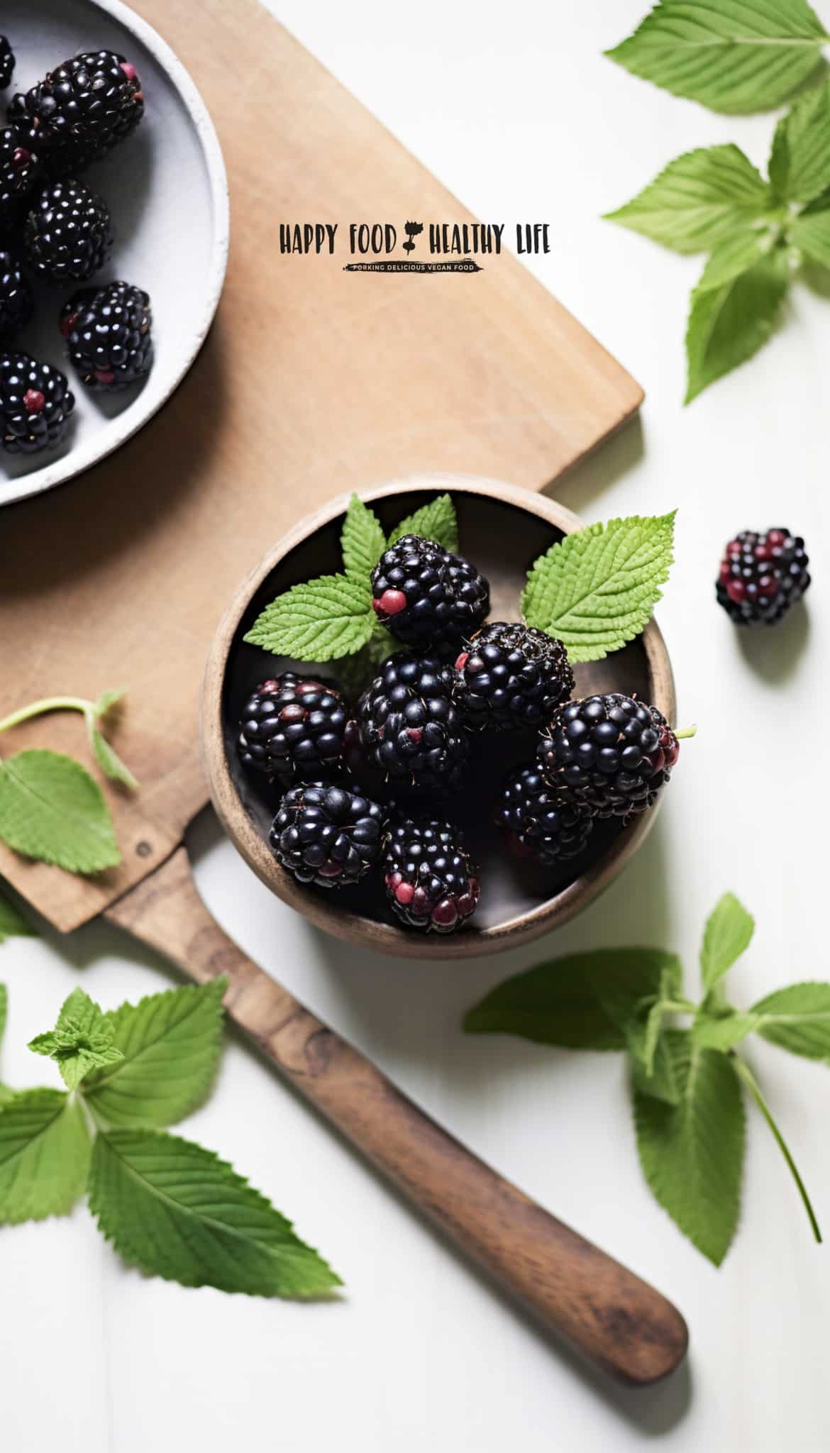overhead shot of fresh blackberries in a bowl with fresh mint spread around. Wooden cutting board in photo