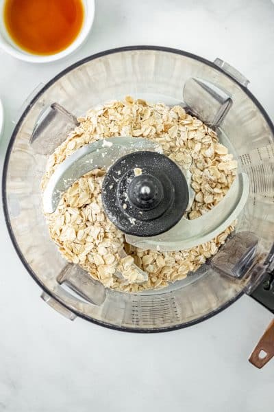 Top view photo of a food processor with oats in the processor. Process until the oats are a fine consistency.
