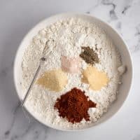 Top view photo of a white bowl with all the spices for vegan fried chicken, ready to mix together for breading.