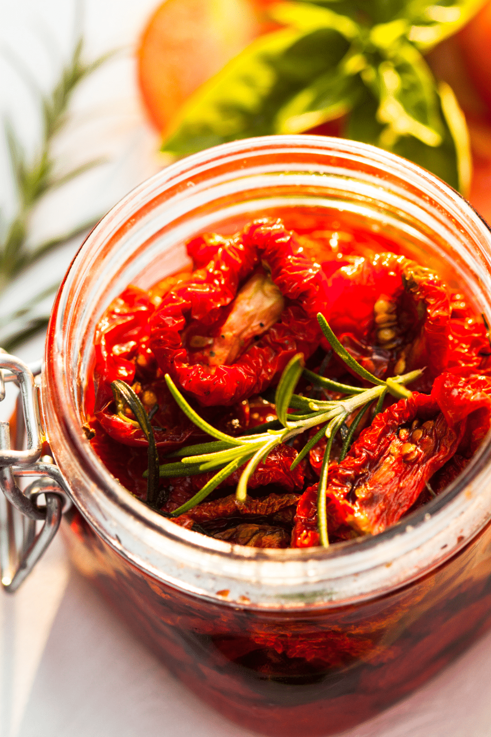 overhead top down shot of sun dried tomatoes in a glass jar and a sprig of rosemary on top