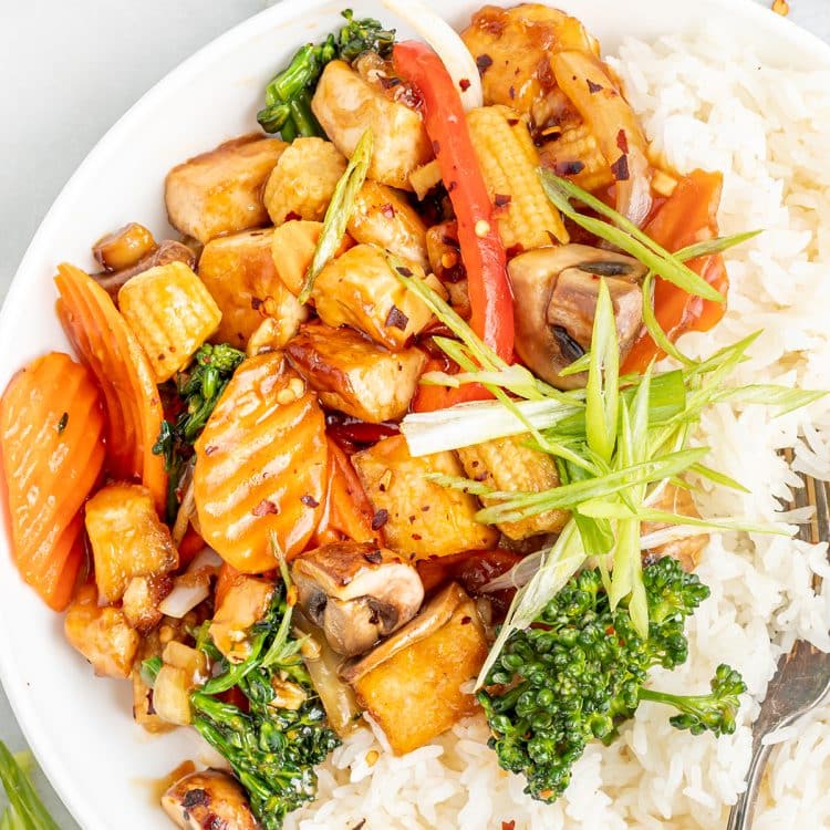 Closeup photo of a white plate with white rice and vegan stir fry on top, ready to enjoy.