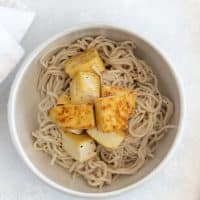 Top view photo of a white bowl with ramen noodles and tofu in the bowl, ready for the vegan ramen broth to be poured on top.