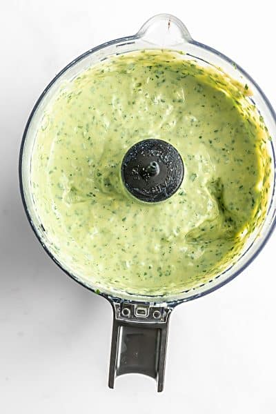 Top view photo of a food processor bowl, with the avocado cream sauce ingredients blended until smooth.