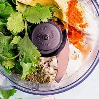 Top view photo of a food processor filled with all the ingredients to make avocado lime ranch dressing, including avocado, dairy-free greek yogurt, egg-less mayo, as well as lime juice and various spices.