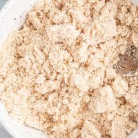 Top view photo of a white bowl filled with the ingredients to make the streusel for the vegan blueberry muffins. It is combined until it forms a sand-like texture. These ingredients include vegan butter, brown sugar, white sugar, sea salt, and gluten-free flour.