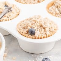 Closeup photo of a muffin tin filled with the vegan blueberry muffins batter and topped with the crumbly streusel topping.