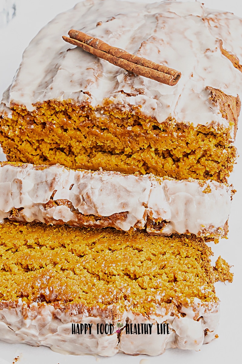 Closeup photo of a vegan pumpkin bread loaf with a maple glaze on top. There is a cinnamon stick on top of the loaf as garnish. 