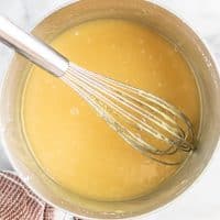 Top view photo of a saucepan filled with the ingredients to make vegan condensed milk, mixed together with a wire whisk.