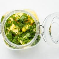 Top view photo of a glass jar filled with pineapple chunks, chopped cilantro, and diced jalapeno in the jar. It is ready for the pickling liquid.