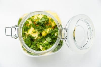 Top view photo of a glass jar filled with pineapple chunks, chopped cilantro, and diced jalapeno in the jar. It is ready for the pickling liquid.