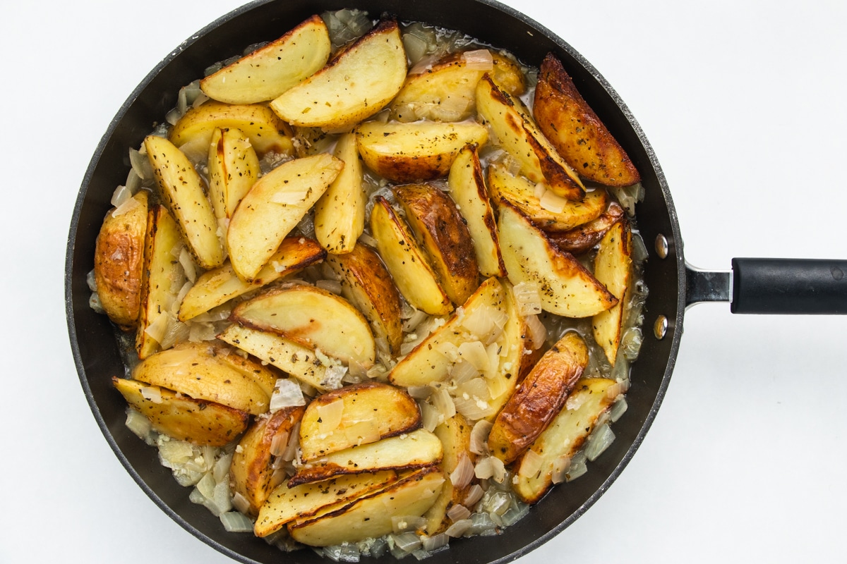 Top view photo of a skillet with the roasted potatoes added to the onion and garlic sauce.