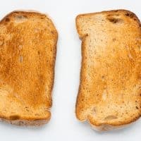 Top view photo of two slices of bread that have been toasted until golden brown. They are on a white tabletop.