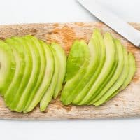 Top view photo of a wooden cutting board, a small knife, and slices of avocado.